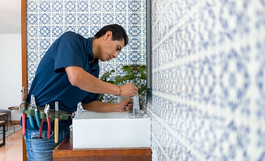 Latin American Plumber fixing a leak in a faucet in a bathroom's sink - home repairment concepts